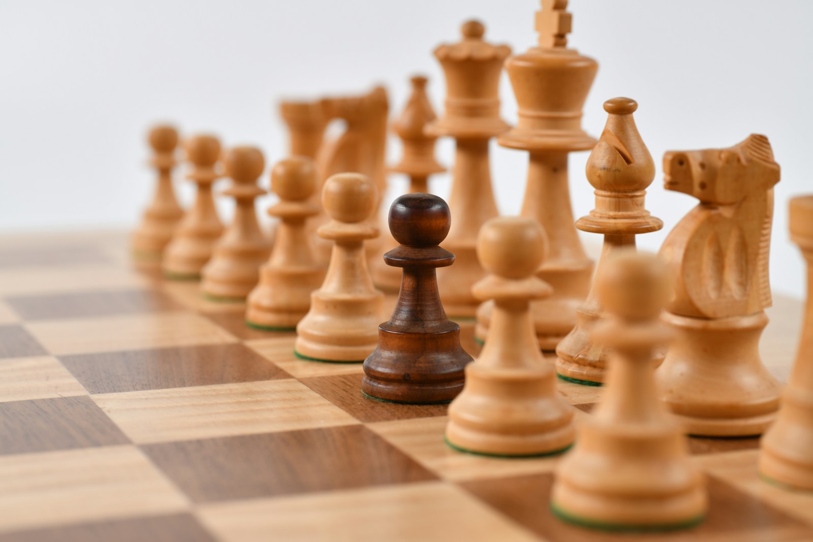 A single dark chess pawn standing among lighter pieces